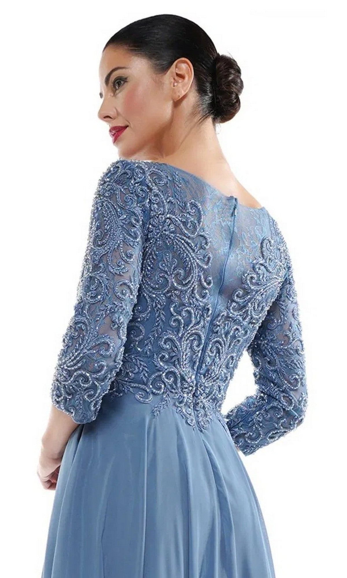 Woman poses with her back turned, hair in a low bun, wearing the Marsoni MV1052—an elegant light blue formal dress featuring embroidery, a beaded bodice, and a flowing chiffon A-line skirt.